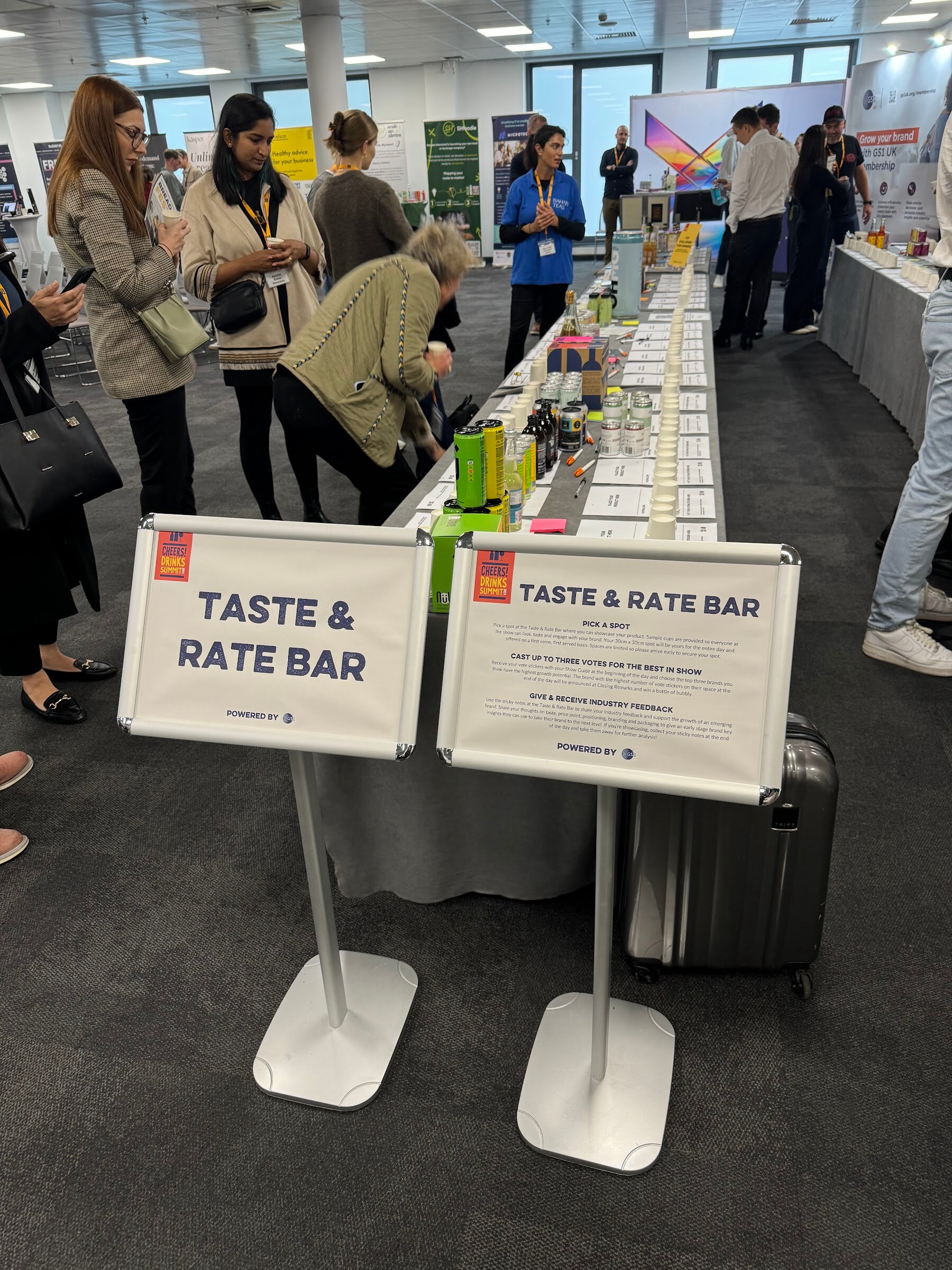 Attendees along a long table of products beside two Taste and Rate Bar signs.