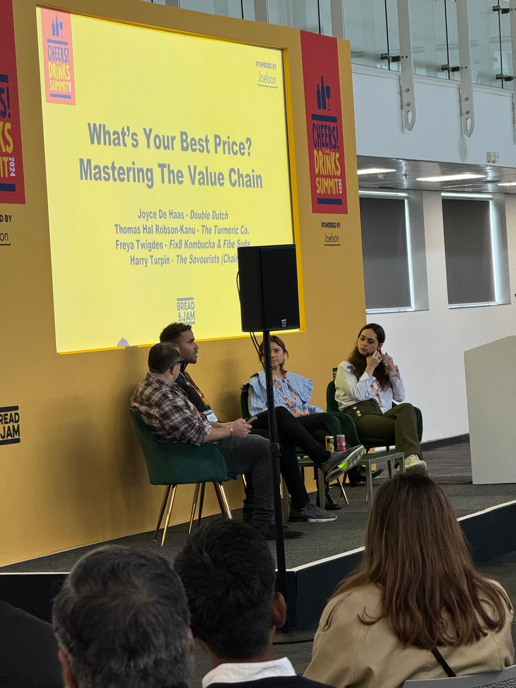 Four panelists in green armchairs on stage beneath a slide titled What's Your Best Price? Mastering The Value Chain.