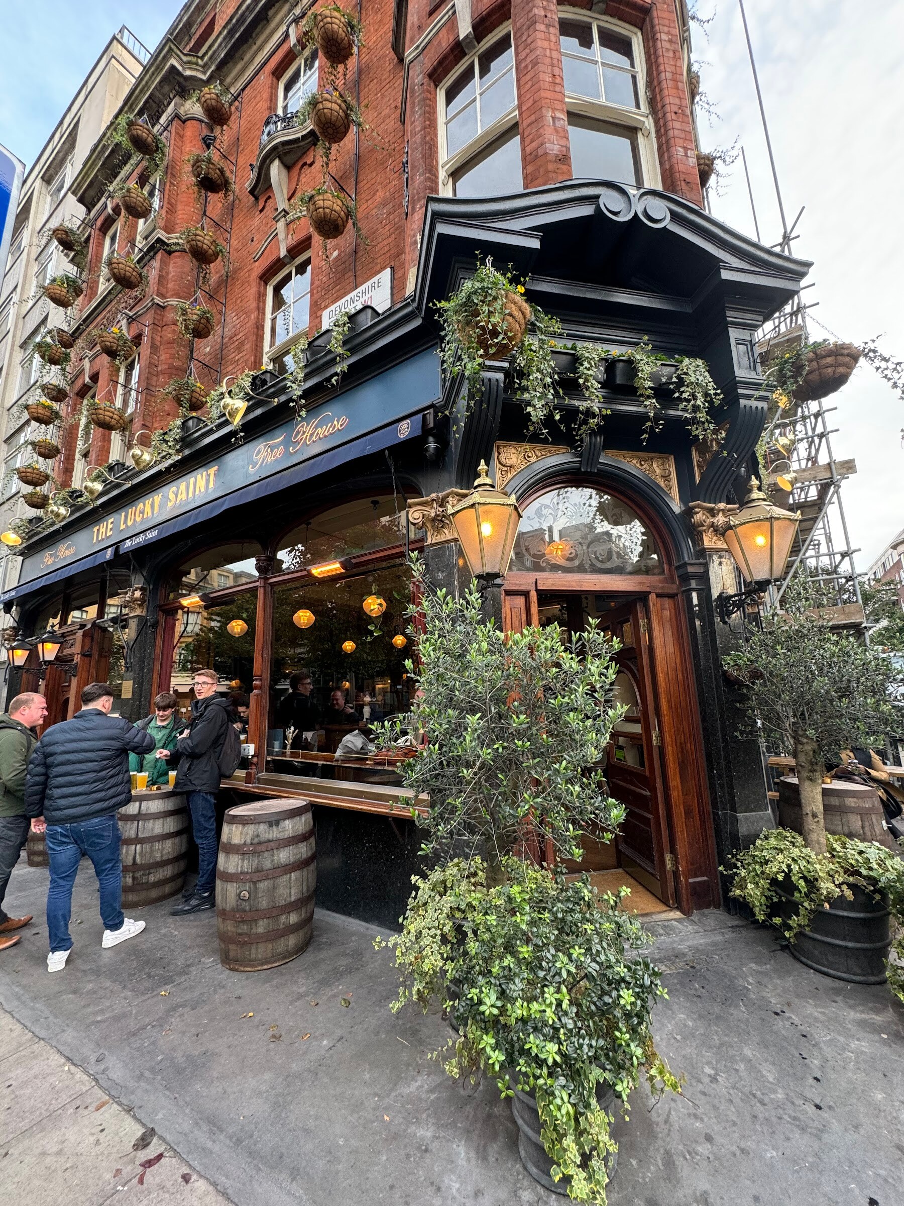 Corner pub with dark timber facade, hanging plants and people standing outside.