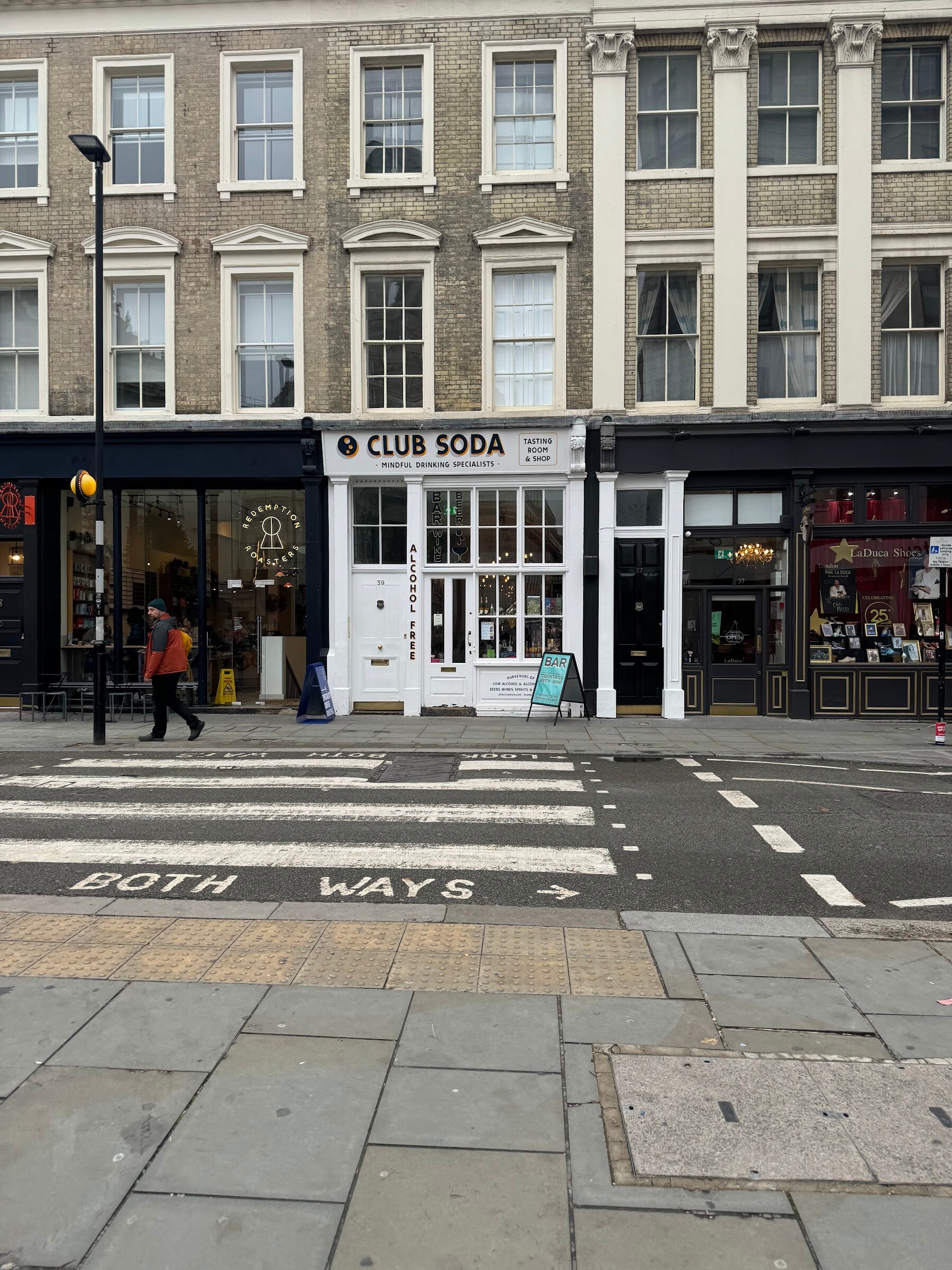 Brick building with a white shop front reading Club Soda across a pedestrian crossing.