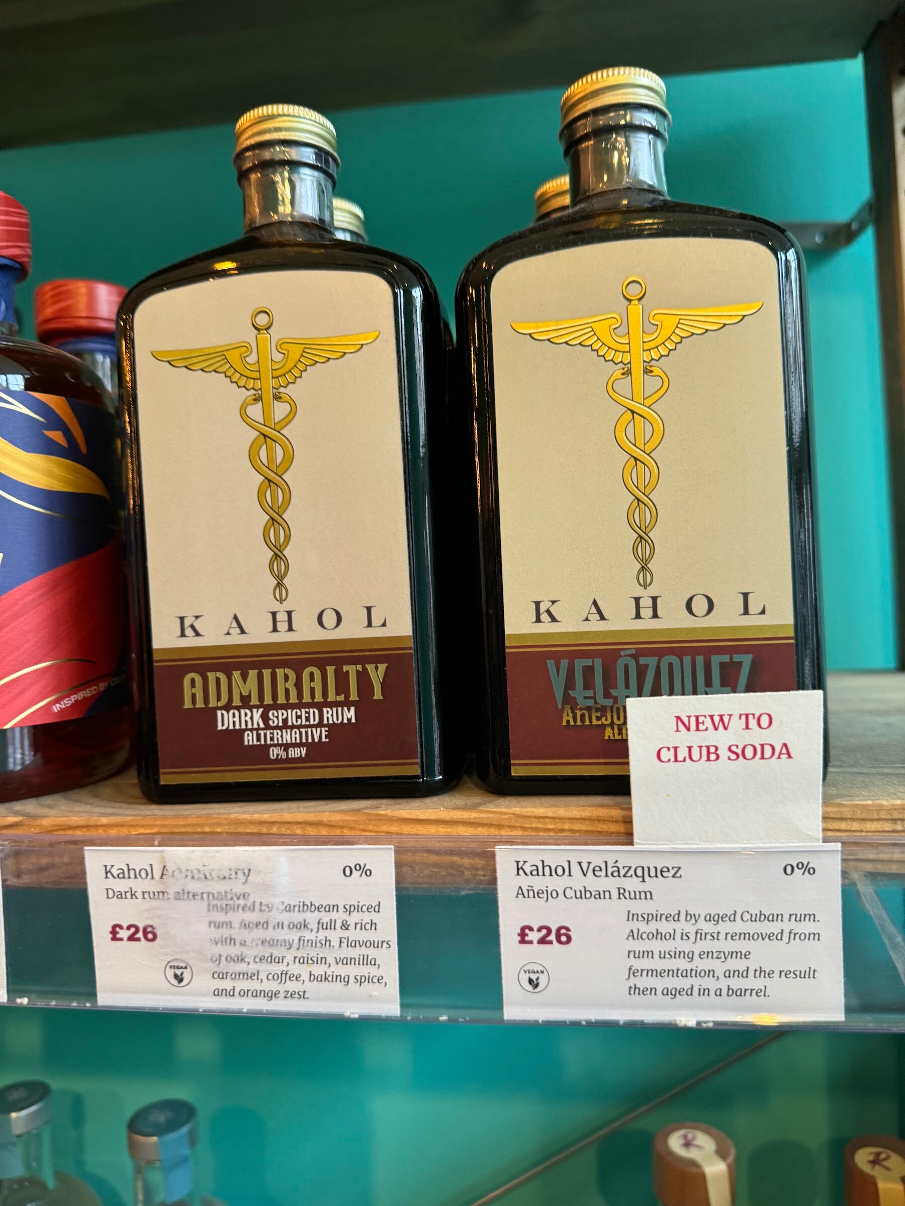 Two dark bottles labeled Kahol Admiralty and Kahol Velazquez on a teal shelf with price cards.