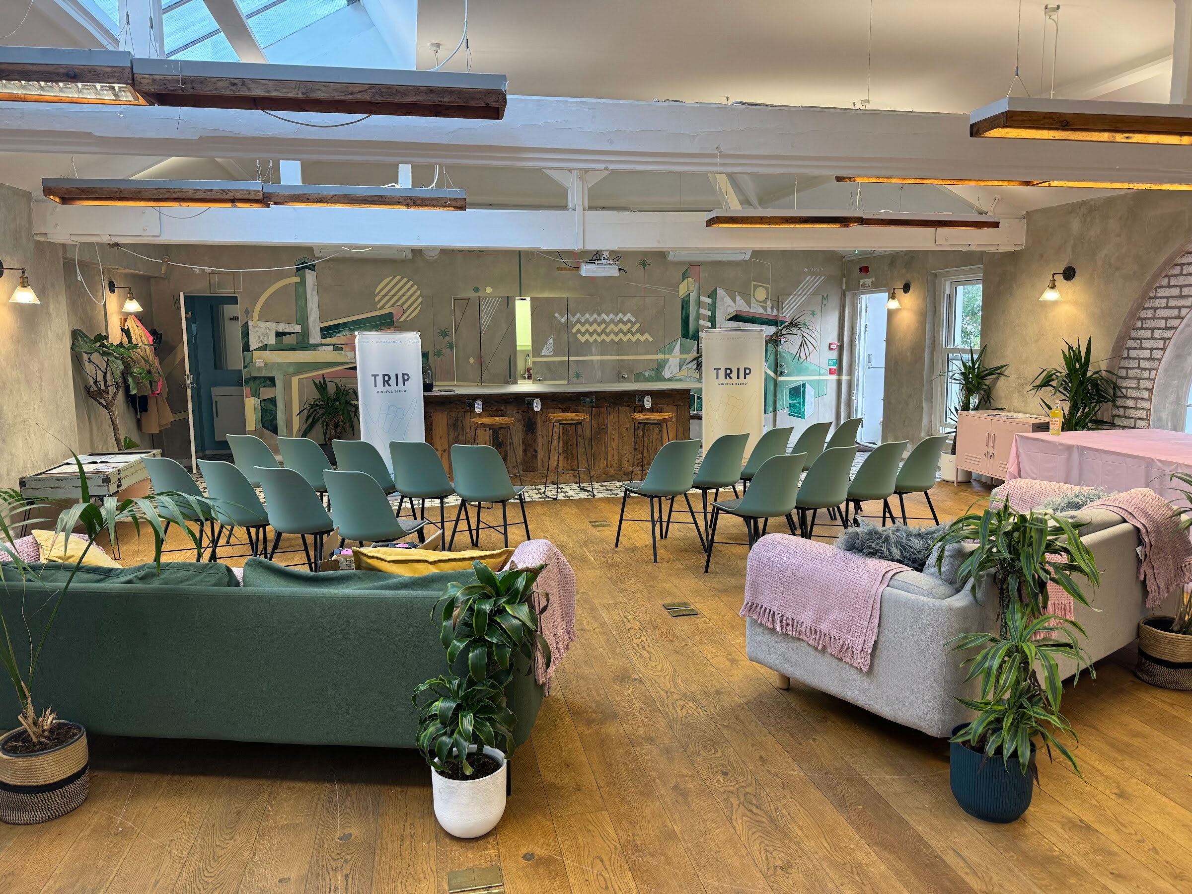 Bright event space with rows of green chairs, sofas, plants and TRIP banners in front of a wooden bar.