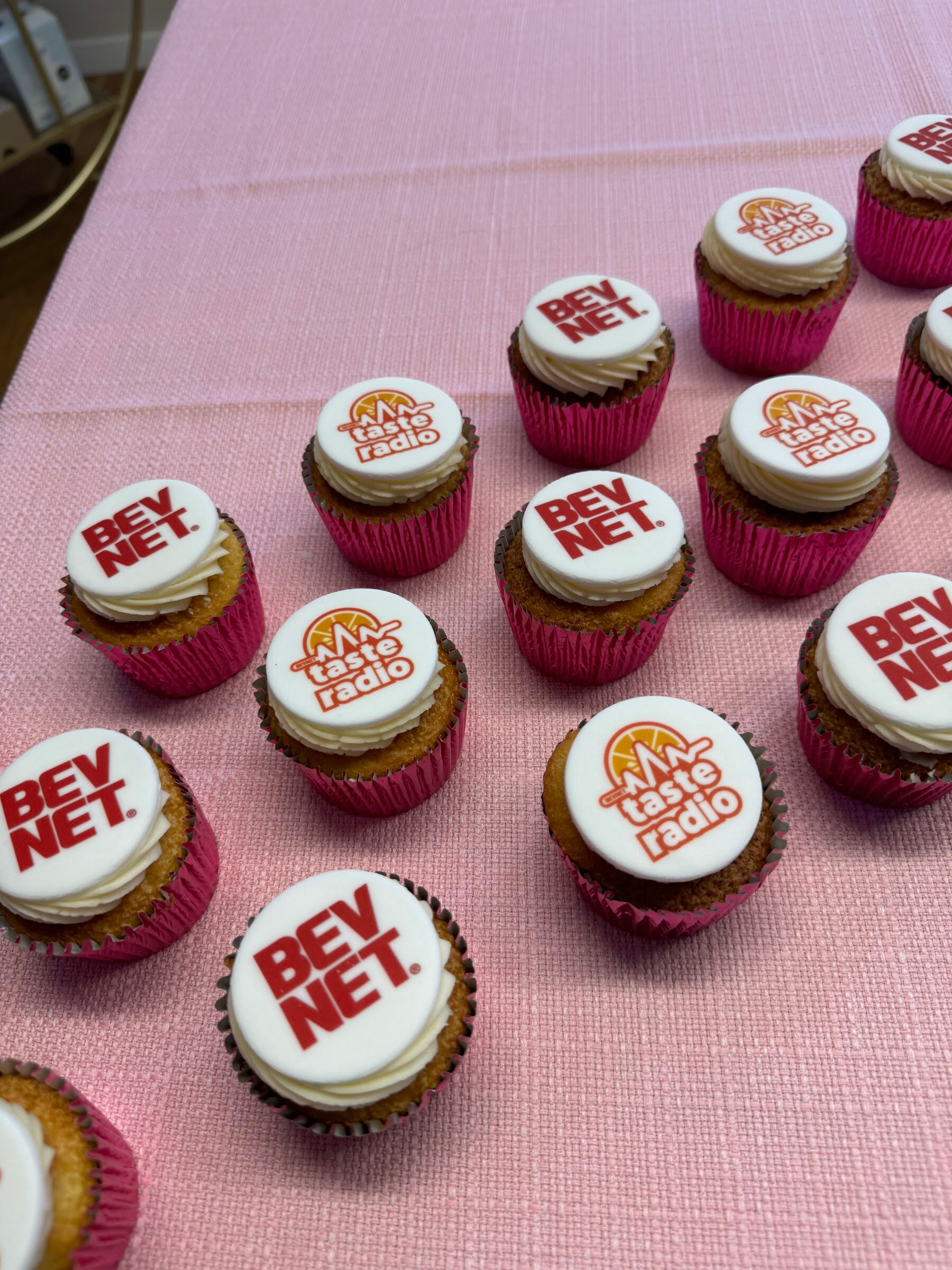 Pink tablecloth covered with cupcakes decorated with BevNET and Taste Radio logos.