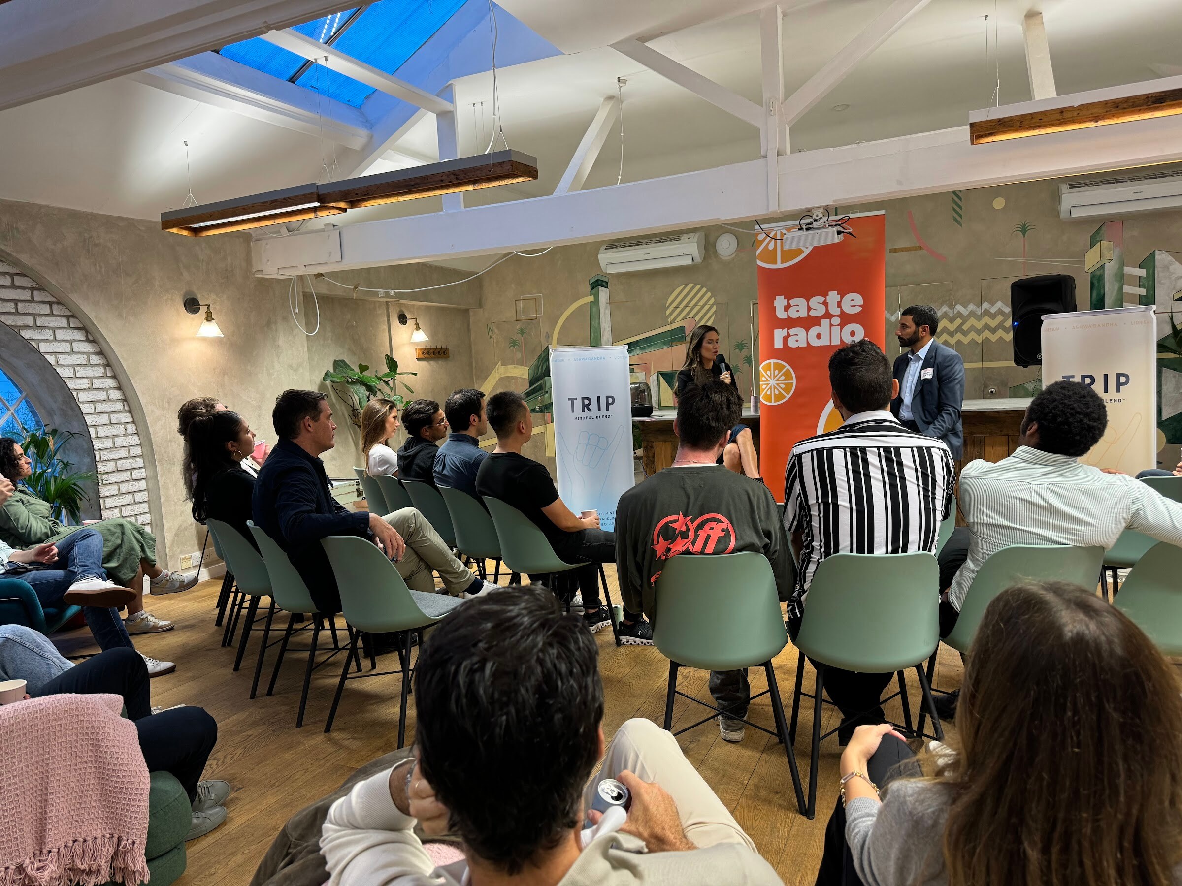 Wide view of the TRIP HQ room under a skylight with a seated audience facing the interviewer and guest.