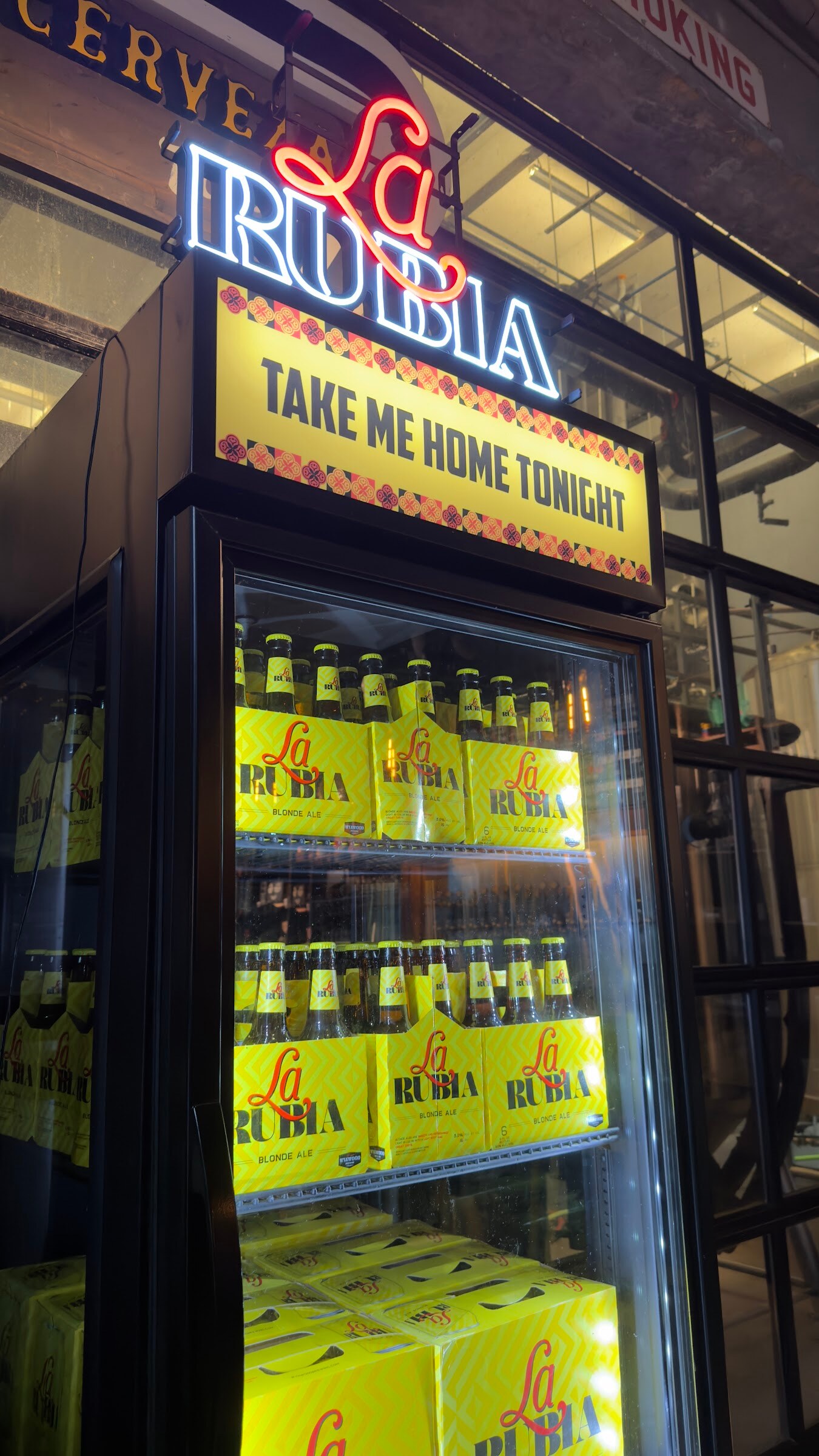 Neon La Rubia sign above a glass-door cooler stocked with yellow cases of La Rubia beer.