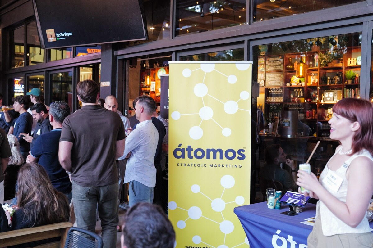 Yellow Átomos Strategic Marketing banner beside attendees, a woman in the foreground holding a drink.