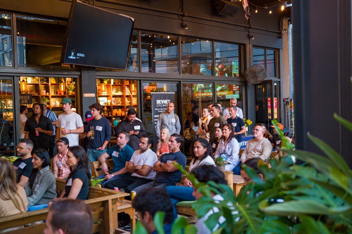 Rows of attendees seated on wooden benches in front of a bar with shelves.