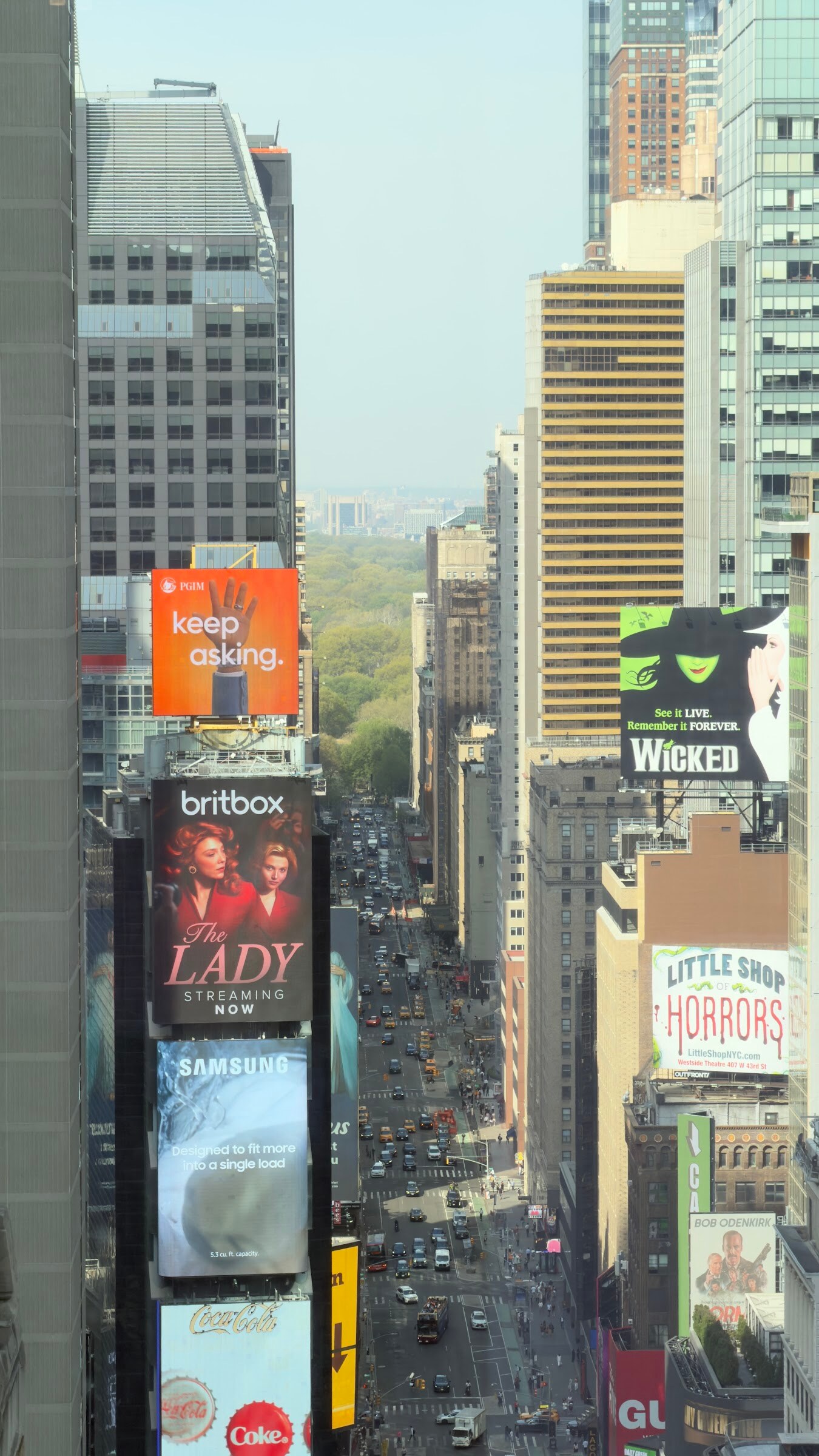 Looking down a Manhattan avenue lined with billboards toward Central Park from a high floor.