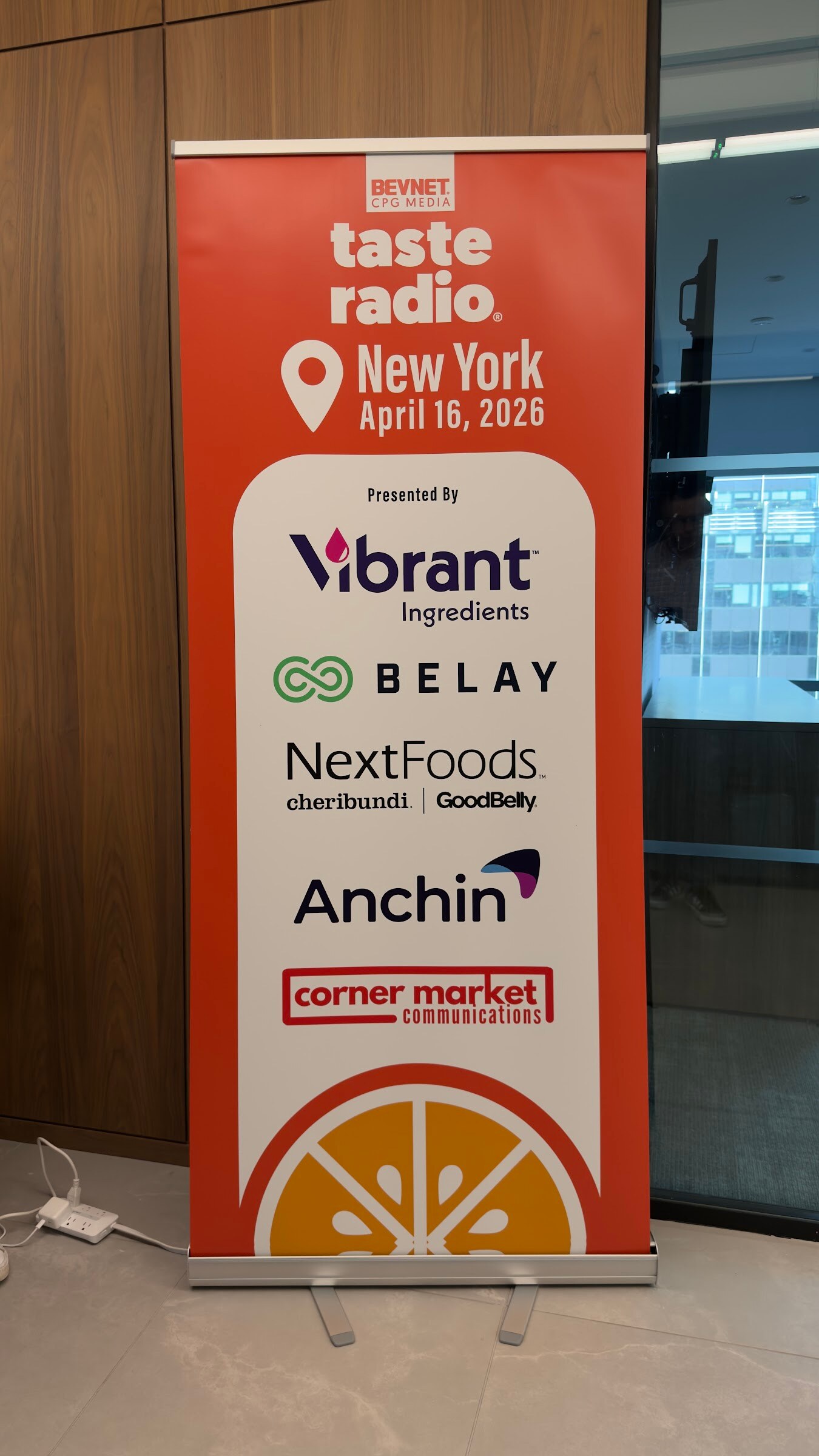 Orange Taste Radio New York April 16, 2026 pull-up banner in an office with wood paneling.