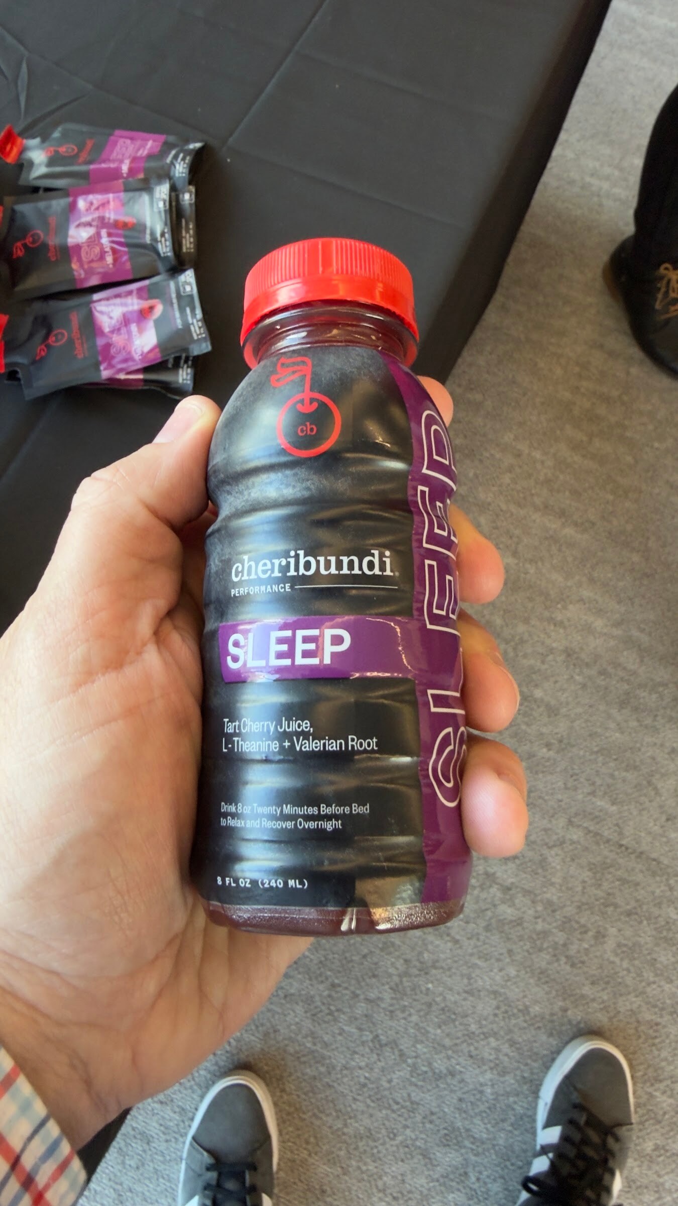 Hand holding a bottle of Cheribundi Sleep tart cherry juice above a table with Cheribundi packets.