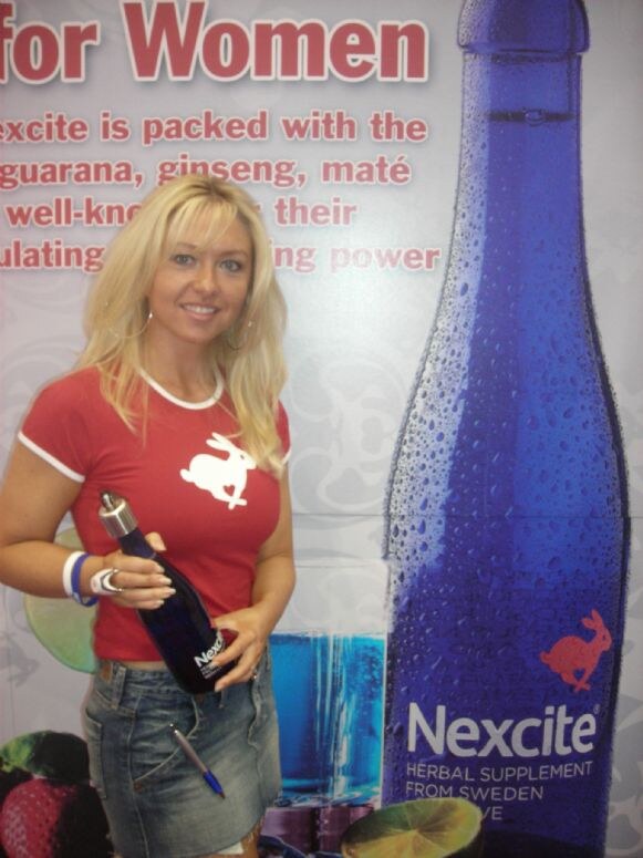 A smiling blonde woman in a red t-shirt with a rabbit logo holds a blue Nexcite bottle beside a large Nexcite bottle graphic and text about the herbal supplement for women.