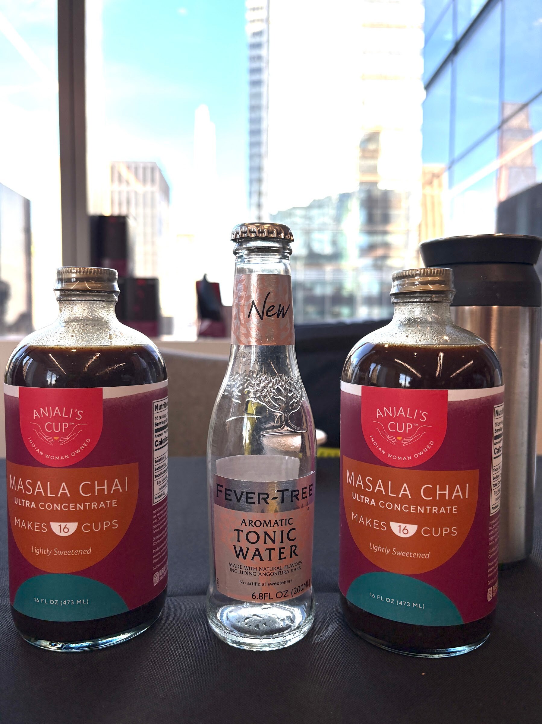 Two bottles of Anjali’s Cup masala chai concentrate flanking a Fever-Tree tonic water bottle in front of a window.