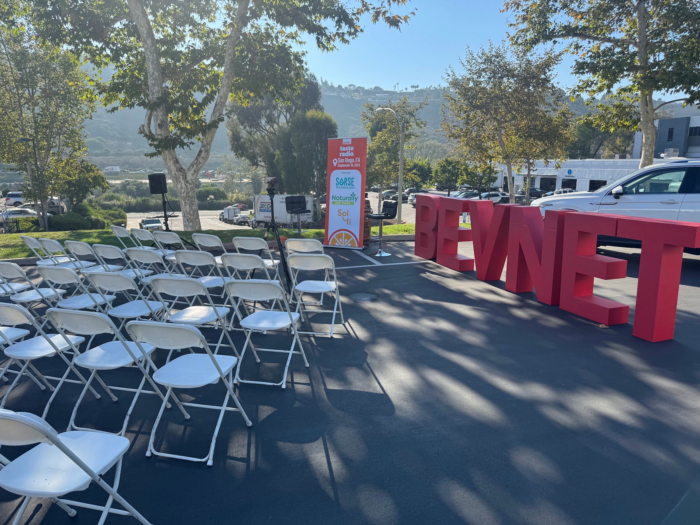 Rows of folding chairs on pavement in front of large red BEVNET letters, with hills behind.