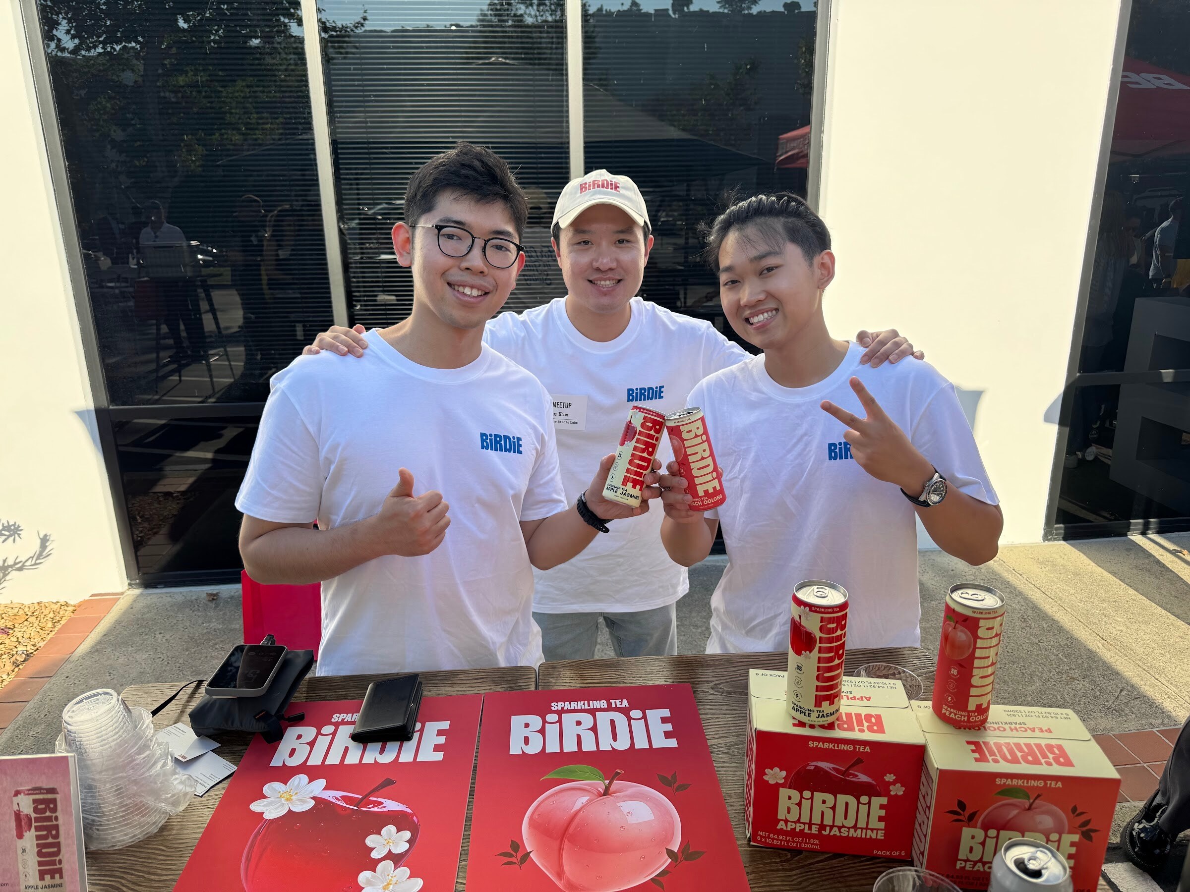 Three men in white T-shirts holding cans of BiRDiE sparkling tea behind a table with BiRDiE signs.