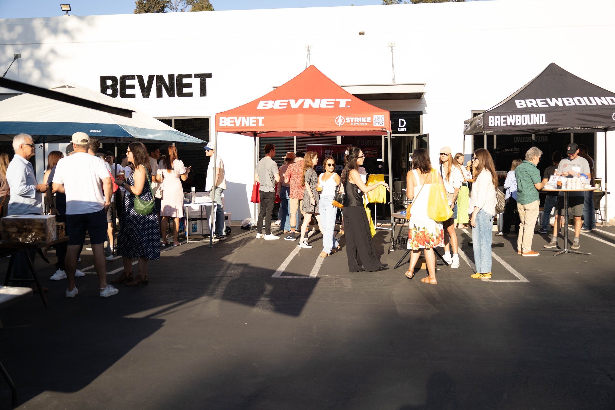 Crowd of attendees in a parking lot beneath red BEVNET and black Brewbound tents.