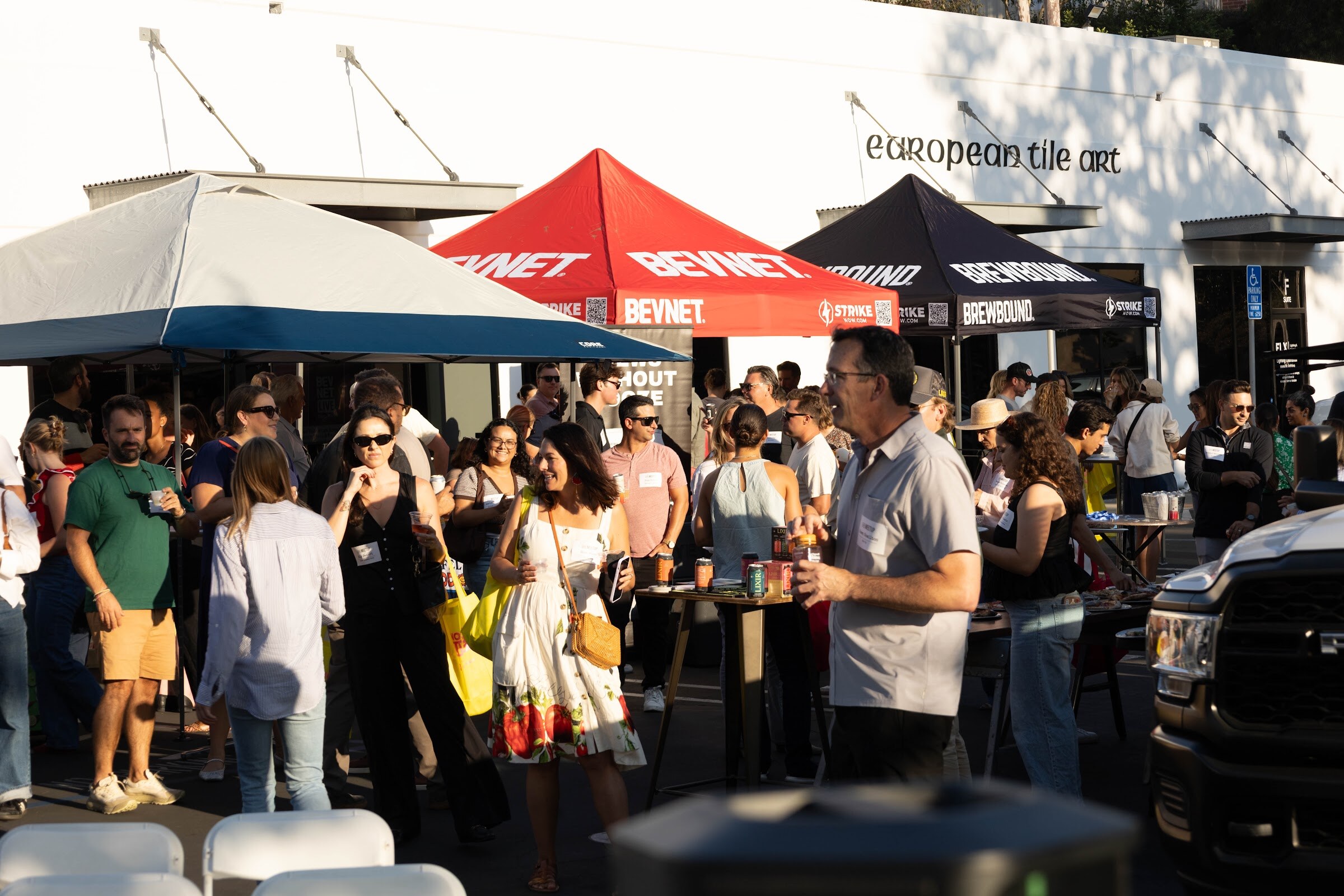 Crowd of attendees mingling in a parking lot under red and black tents.