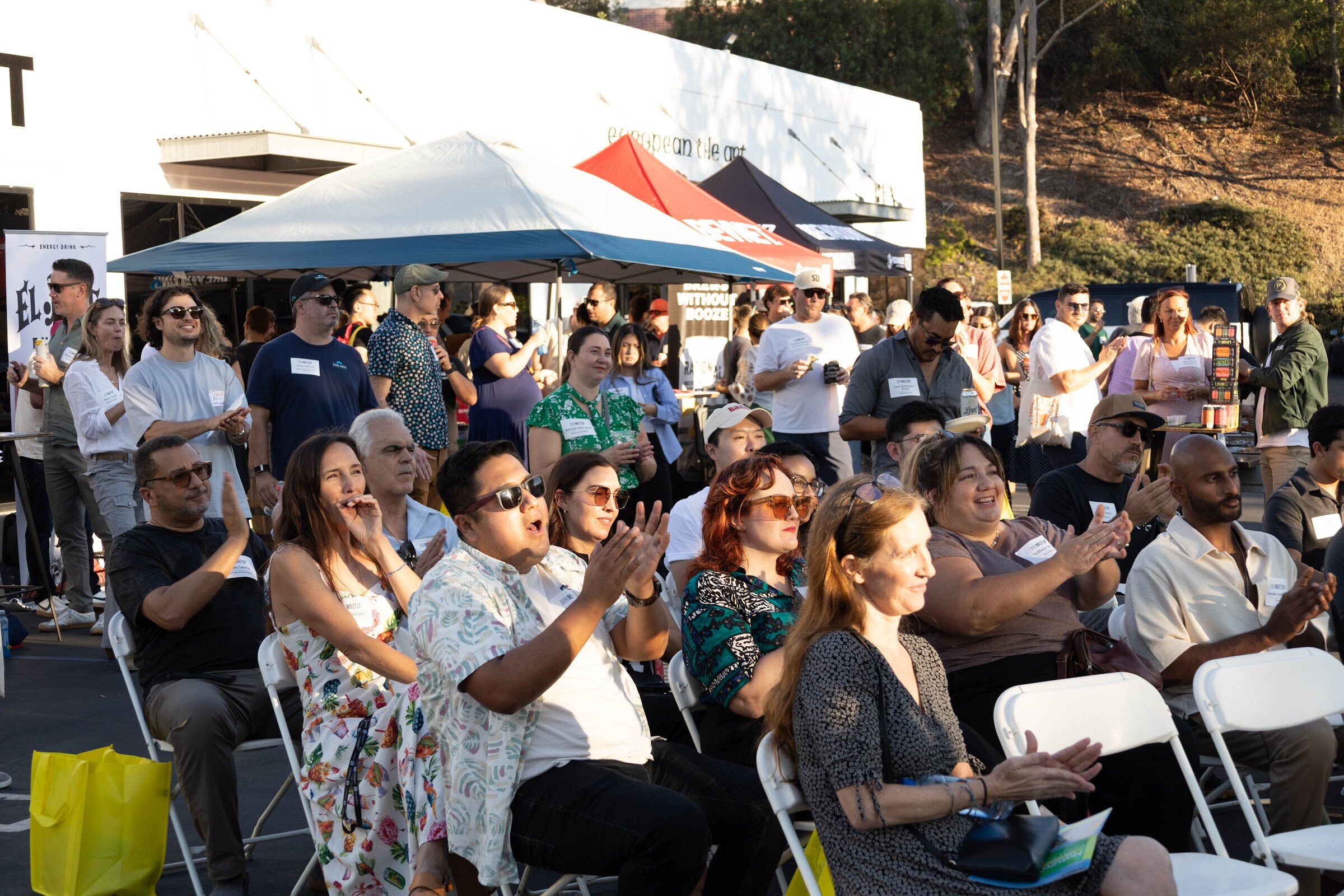 Seated audience members smiling and applauding, with a crowd standing behind them.