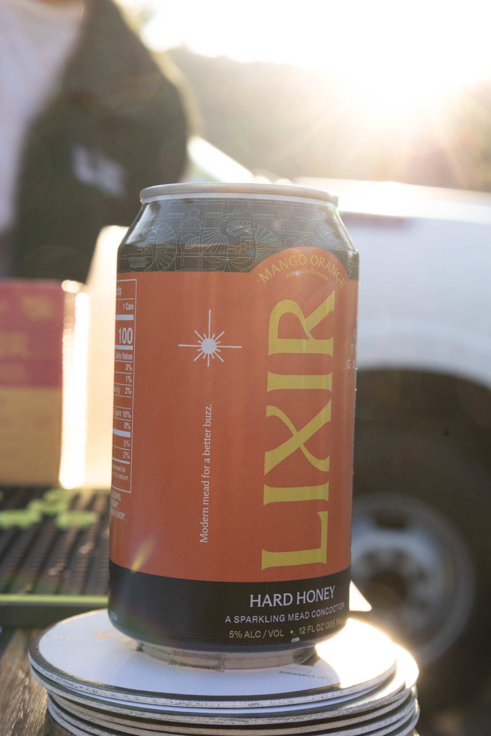 Can of Lixir hard honey standing on a stack of coasters in backlight.
