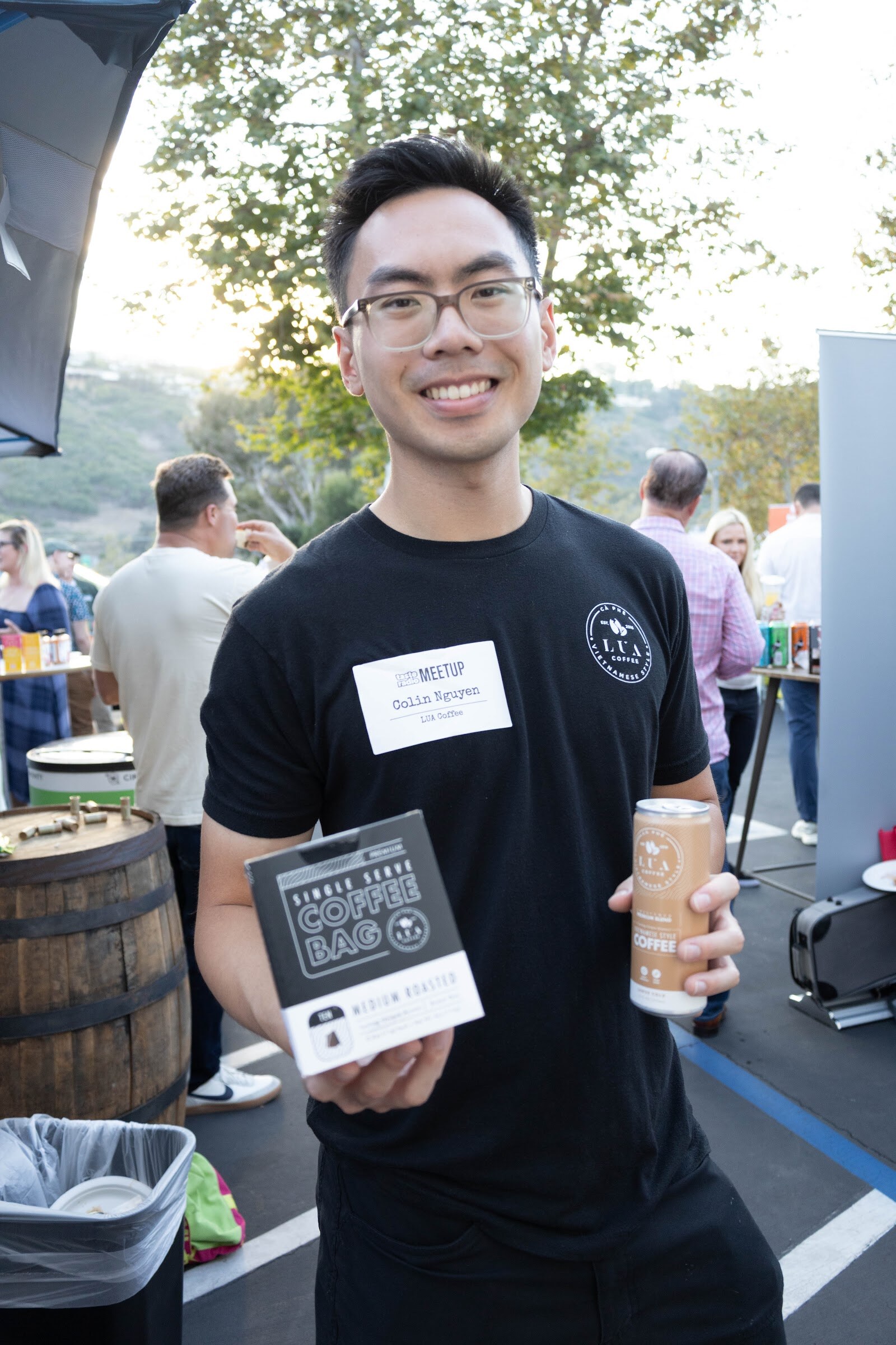 Smiling man in glasses and a black shirt holding a small box and a can.