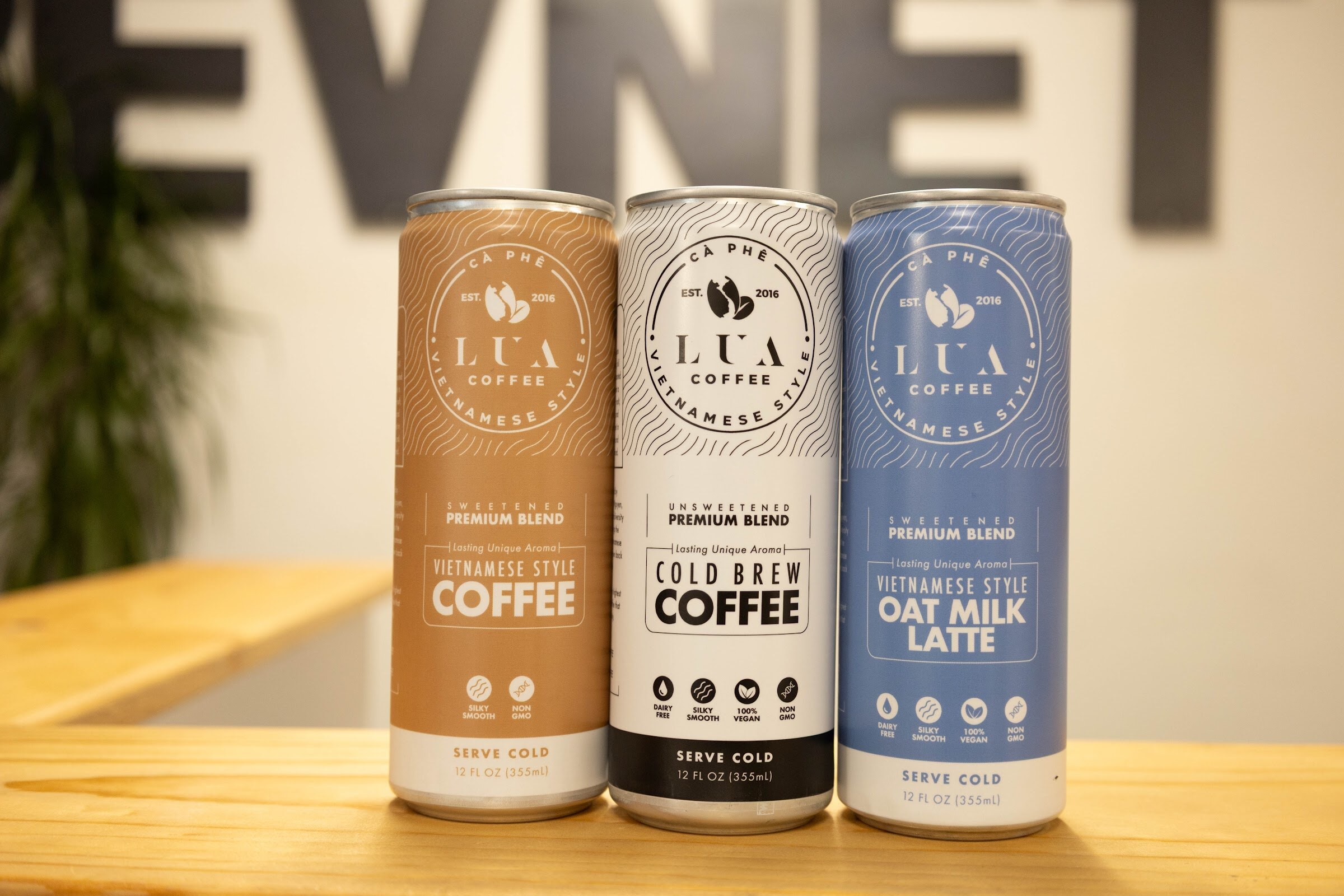 Three Lua Coffee cans in front of a blurred BEVNET sign.