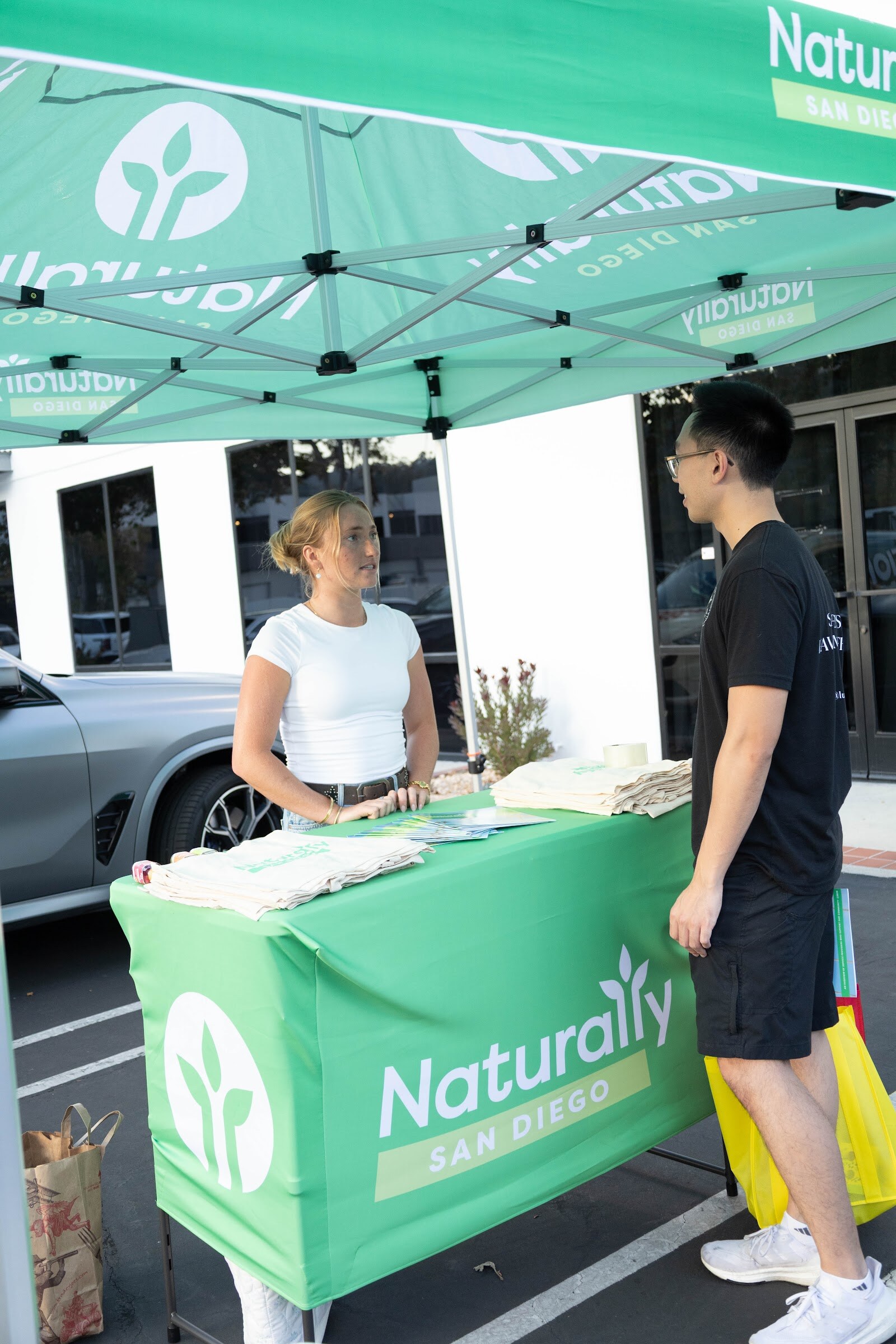 Two people talking beside a green Naturally San Diego tent and tablecloth.