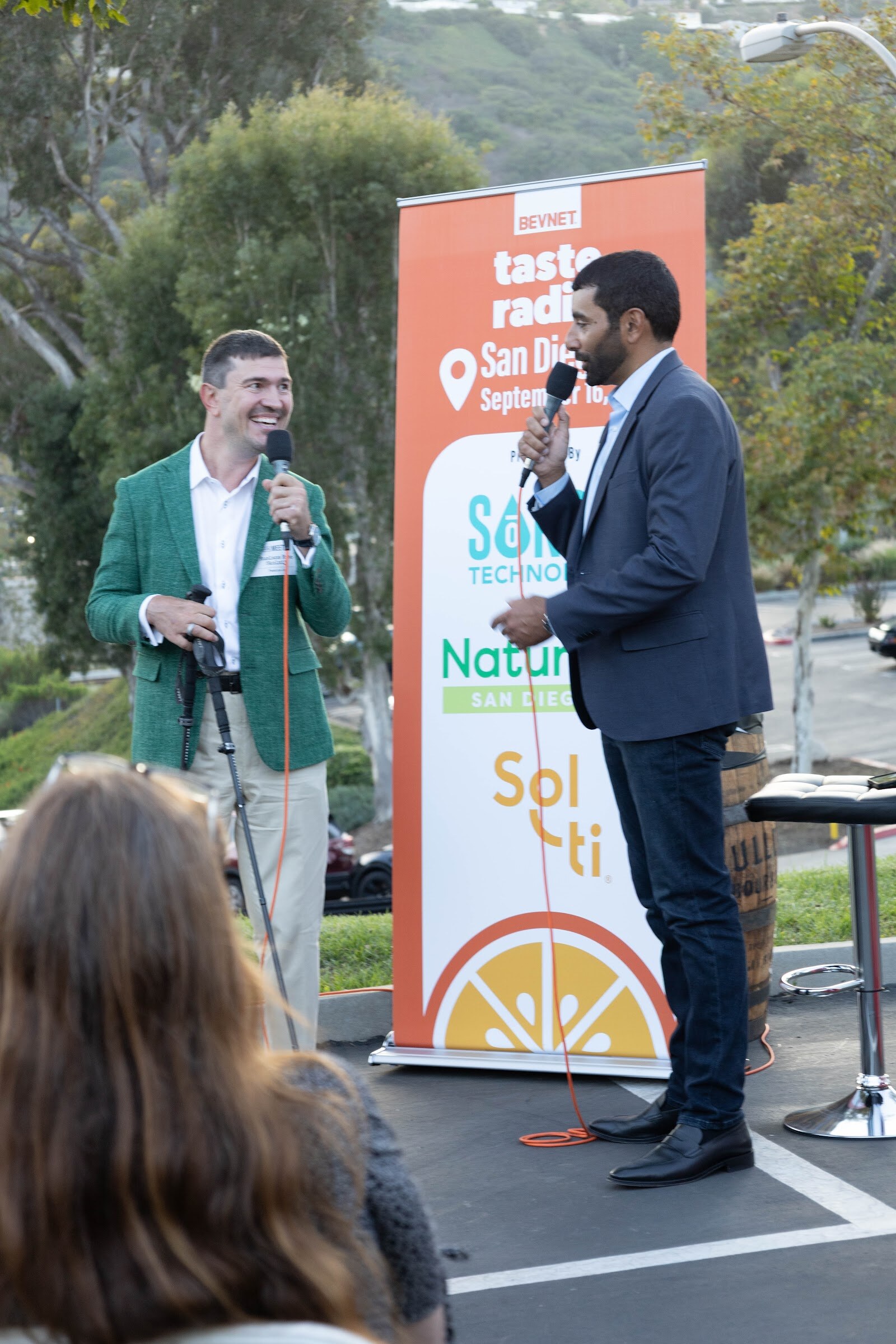 Man in a green blazer and the host in a suit standing by the Taste Radio banner.