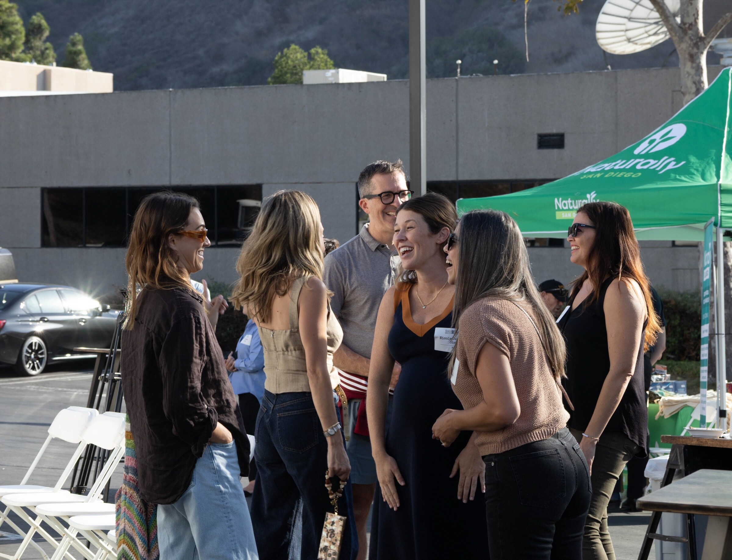 Six attendees laughing together in a circle next to a green Naturally San Diego canopy.