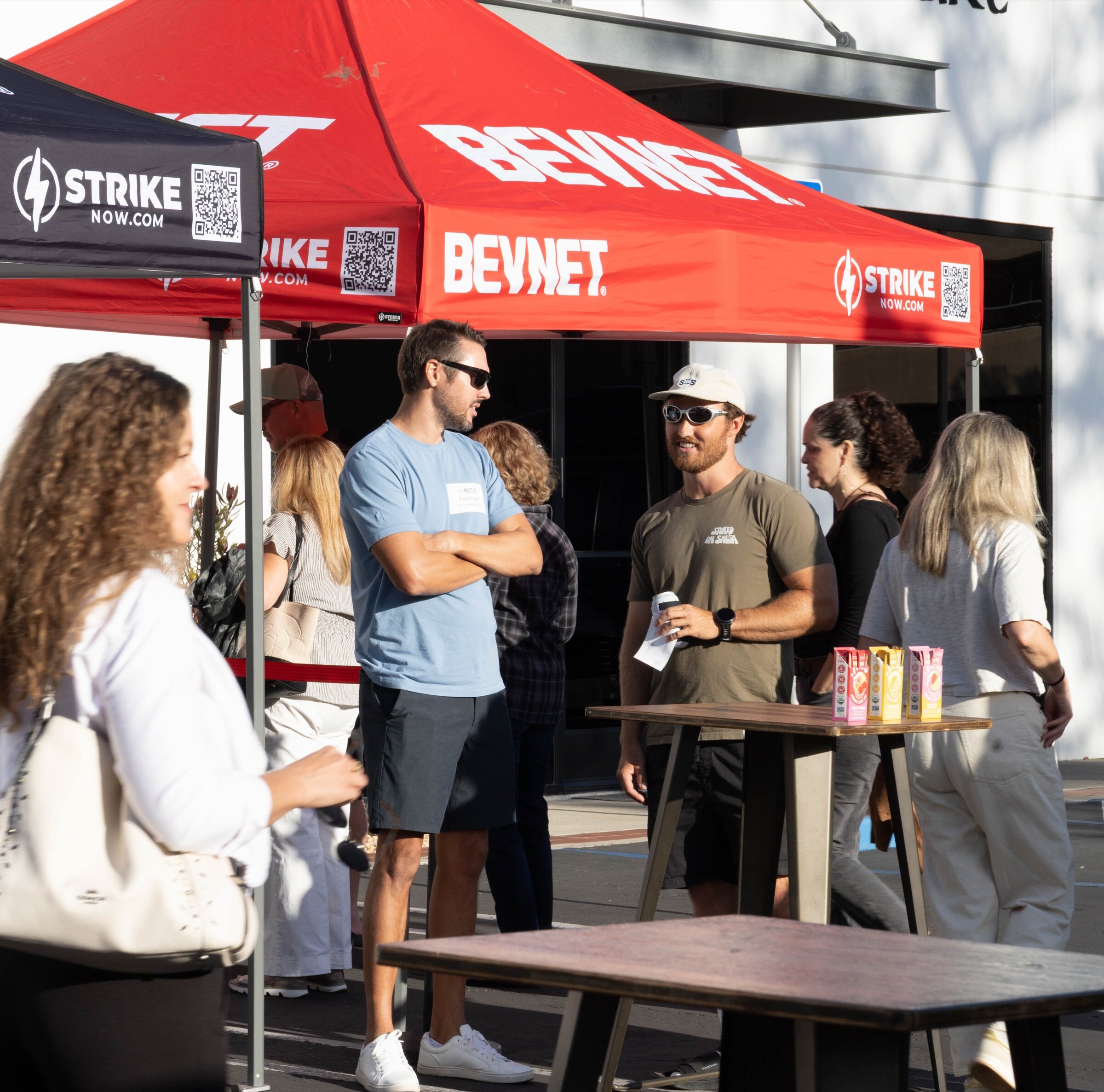 Attendees stand and talk beneath red BevNET and black Strike canopies, with drink cartons on a high-top table.