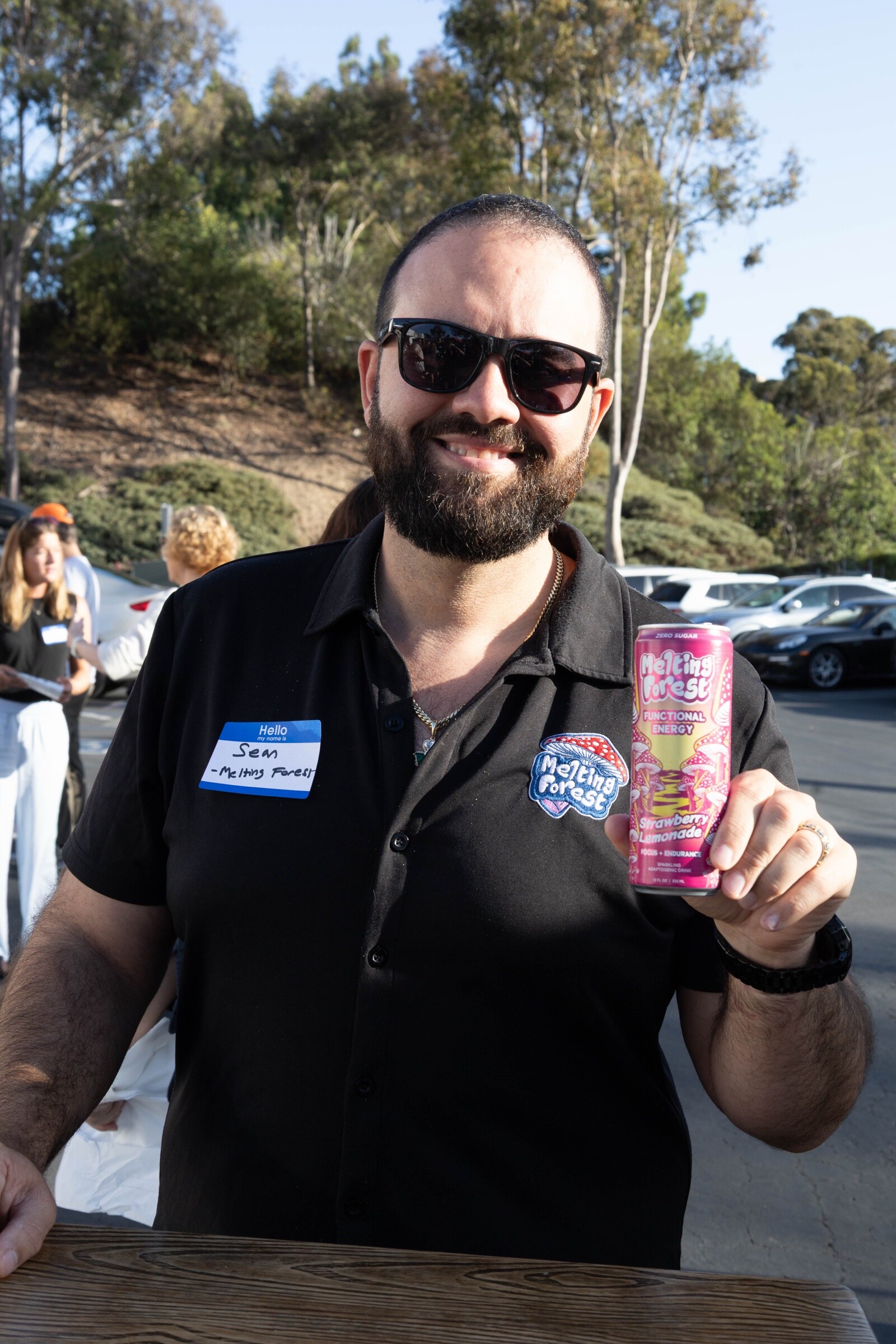 Bearded man in a Melting Forest shirt and sunglasses holds up a can of Melting Forest Strawberry Lemonade functional energy.