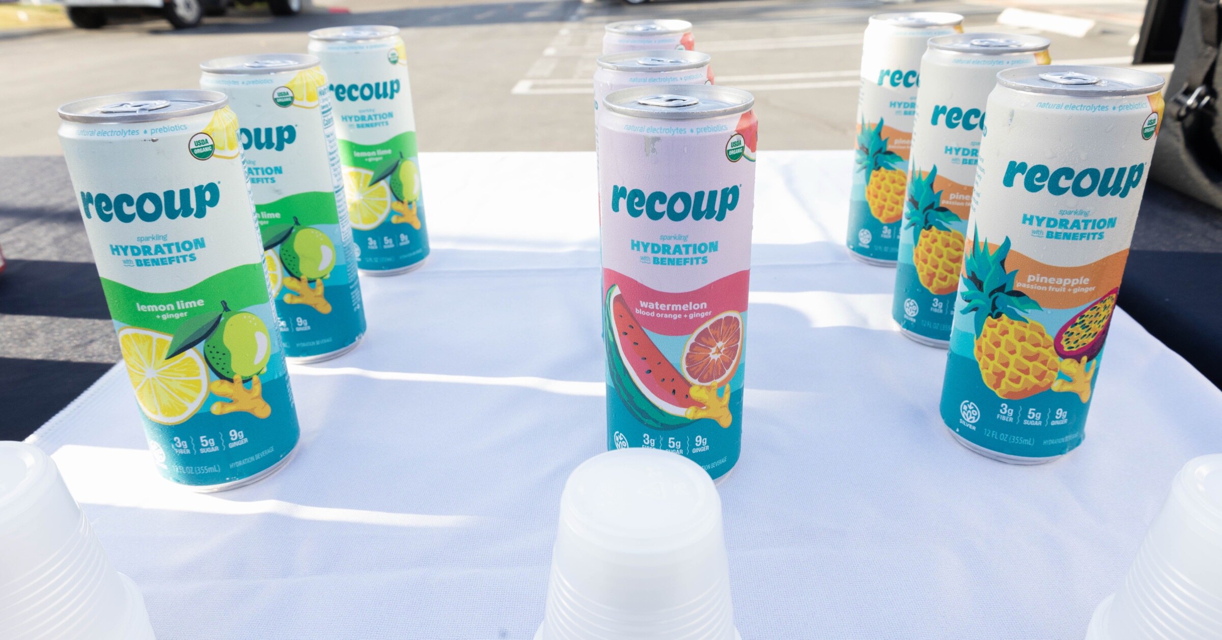 Cans of Recoup hydration drinks standing on a white tablecloth.
