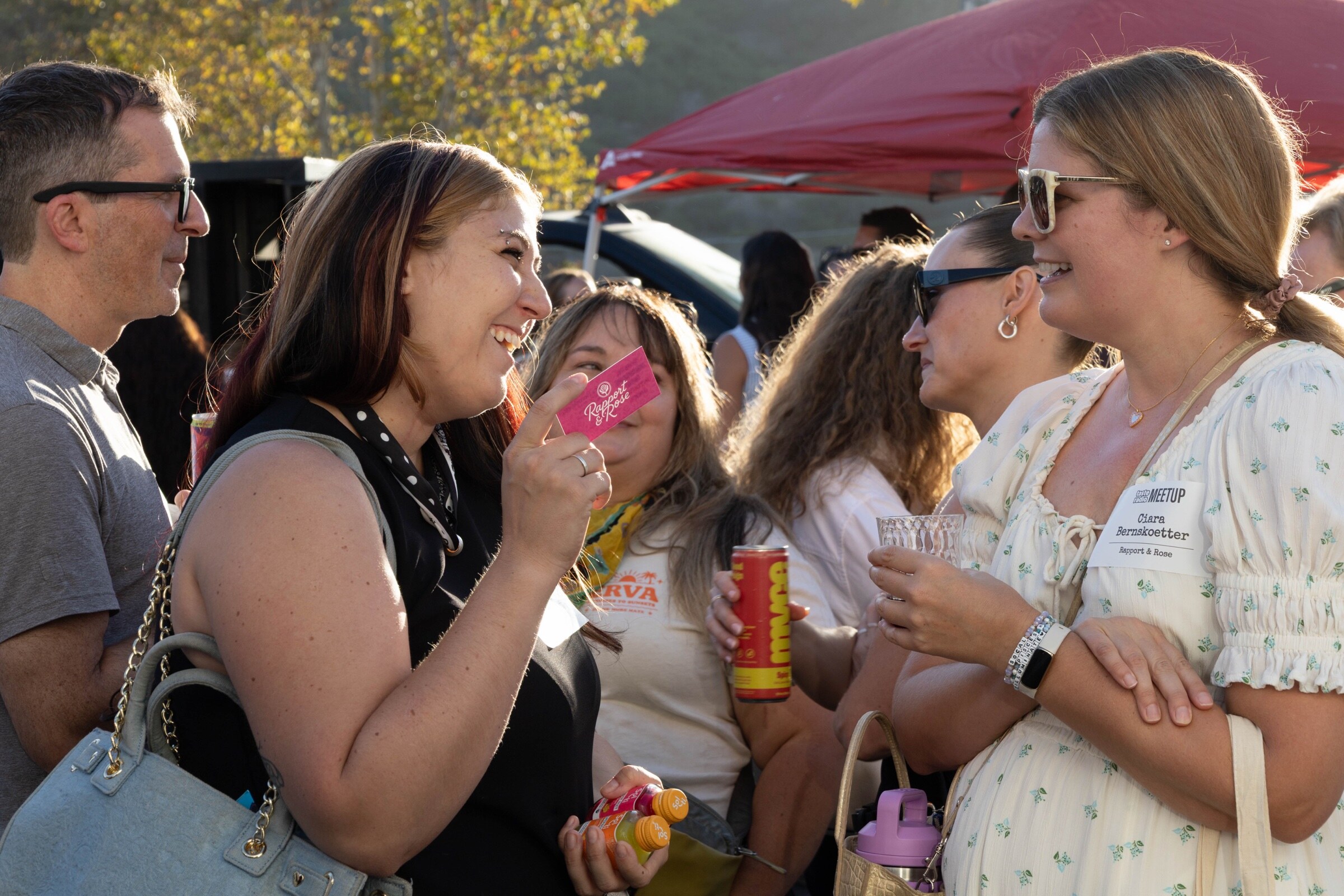 Several women laugh together, one holding a business card and another holding a can.