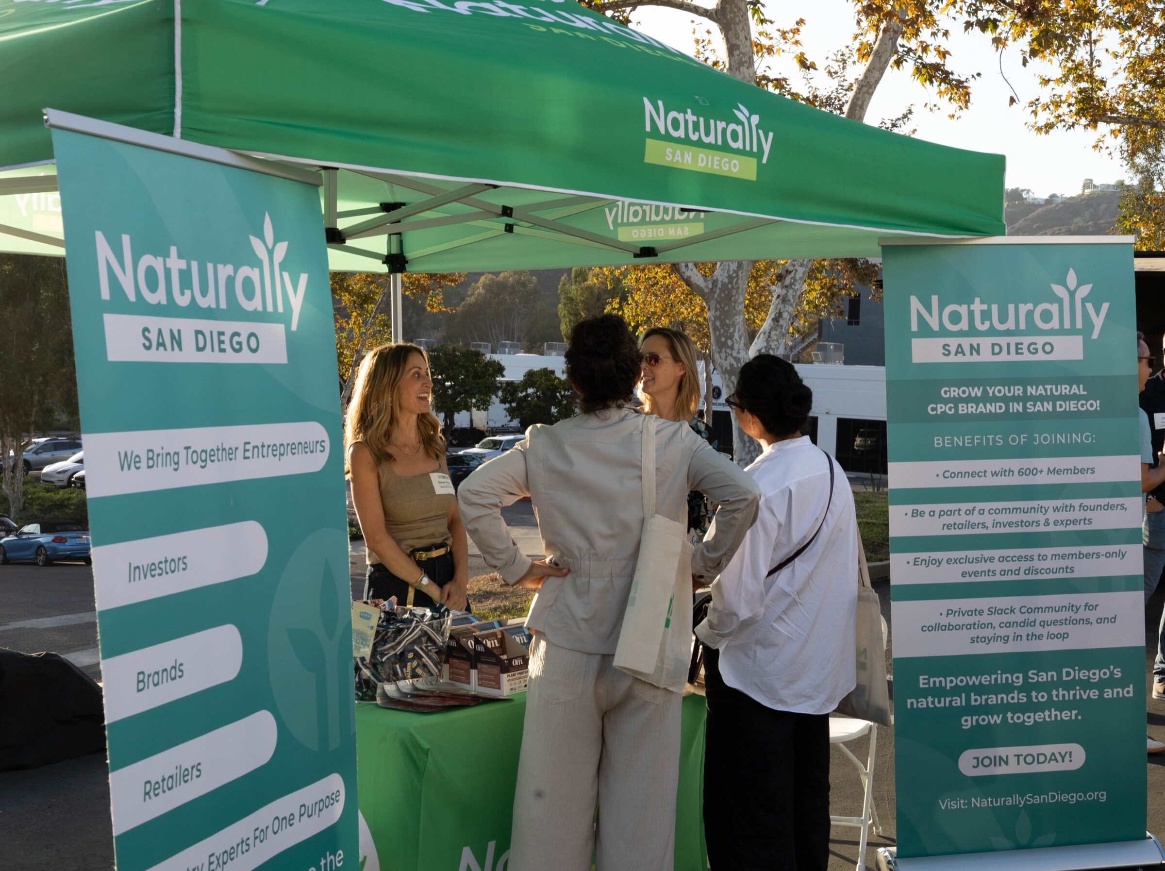 Green Naturally San Diego canopy with two teal banners as a representative talks with three attendees.