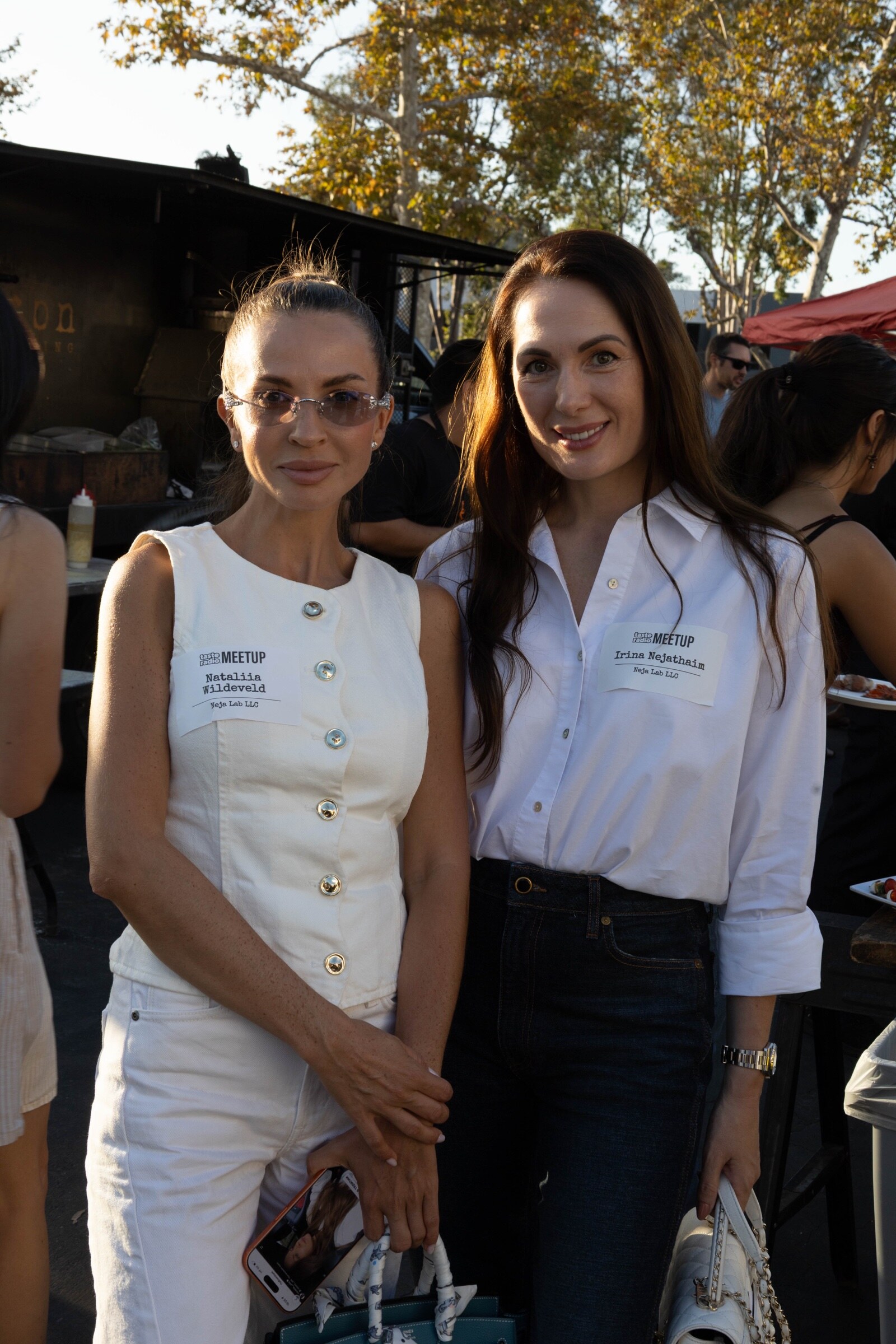 Two women in white tops pose side by side in the evening sun.