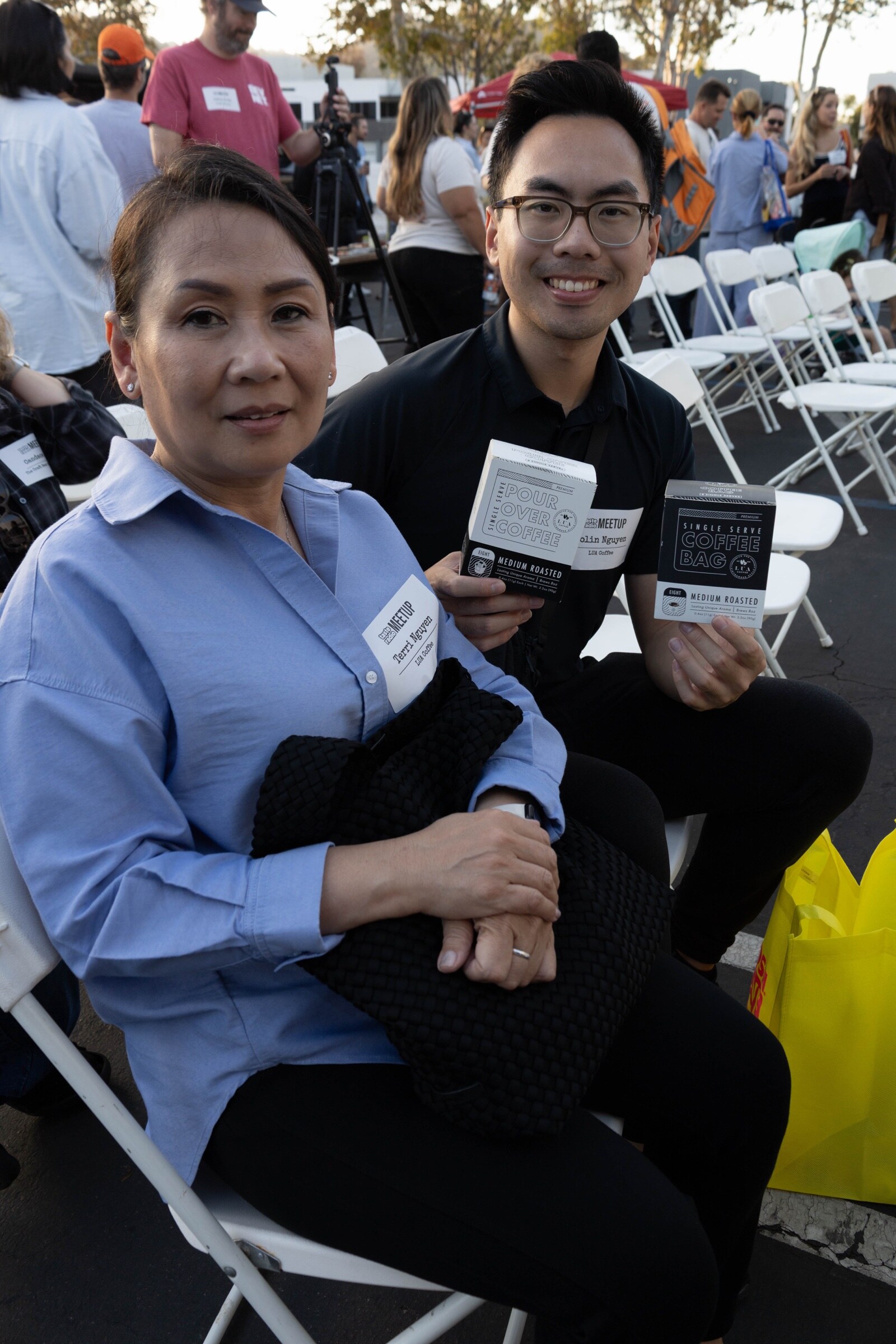 Seated woman and man smile, the man holding boxes of LUA single-serve pour-over coffee and coffee bags.